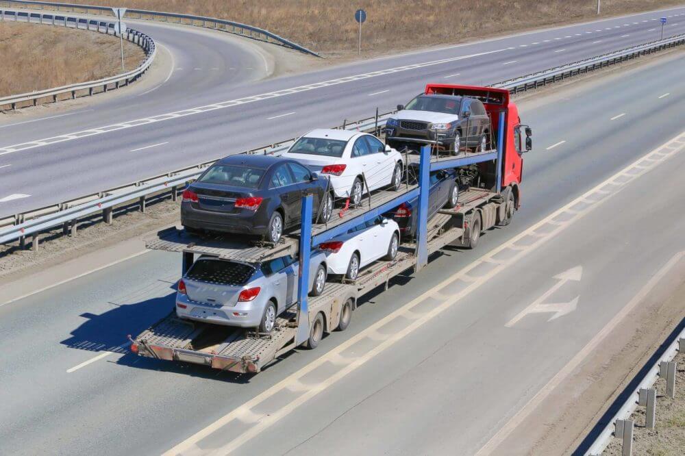 A truck with cars in the open trailer on the road 