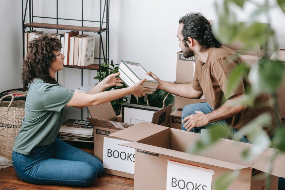 a couple is boxing up books for long-distance moving 