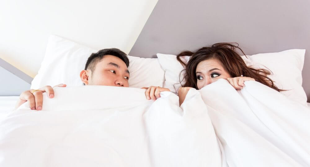 A couple looking at each other, covered with bed sheets