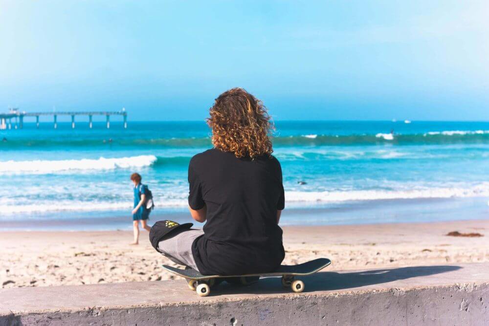 A person sitting on a skateboard observing the sea
