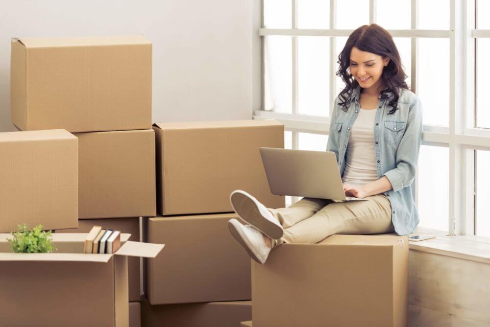 Young woman typing on the laptop, surrounded by boxes