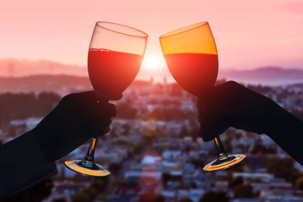 Man and woman clanging wine glasses with champagne at sunset 
