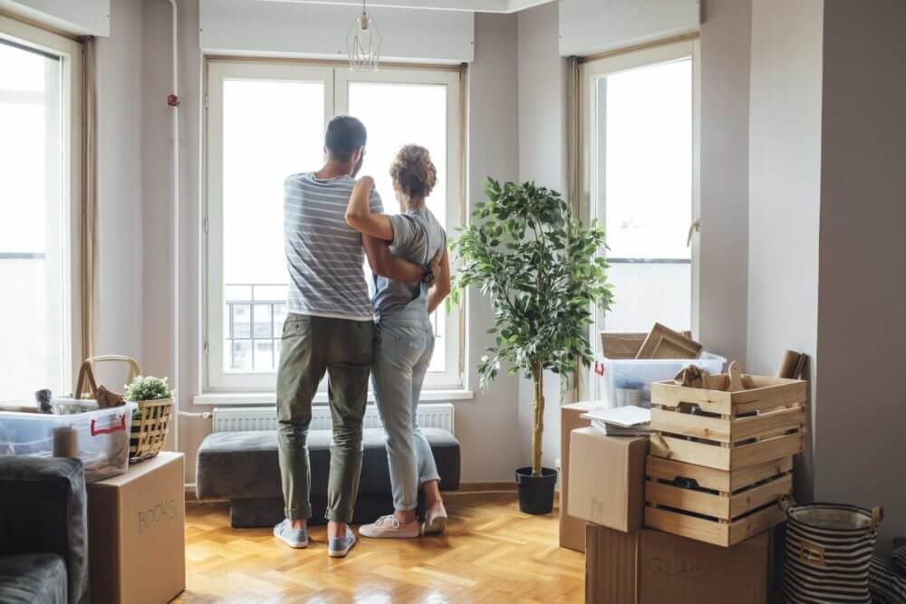 Happy couple hugging looking through the window in living room