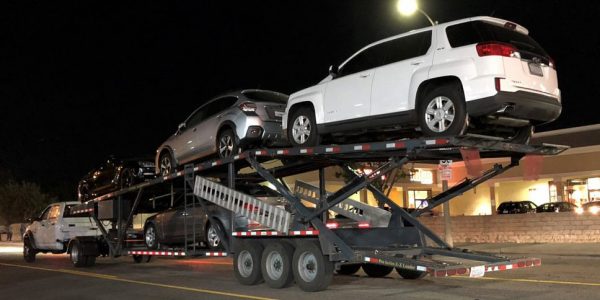 Long-distance movers shipping cars on an open trailer