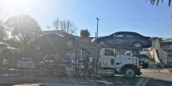 Long-distance movers shipping cars on an open trailer