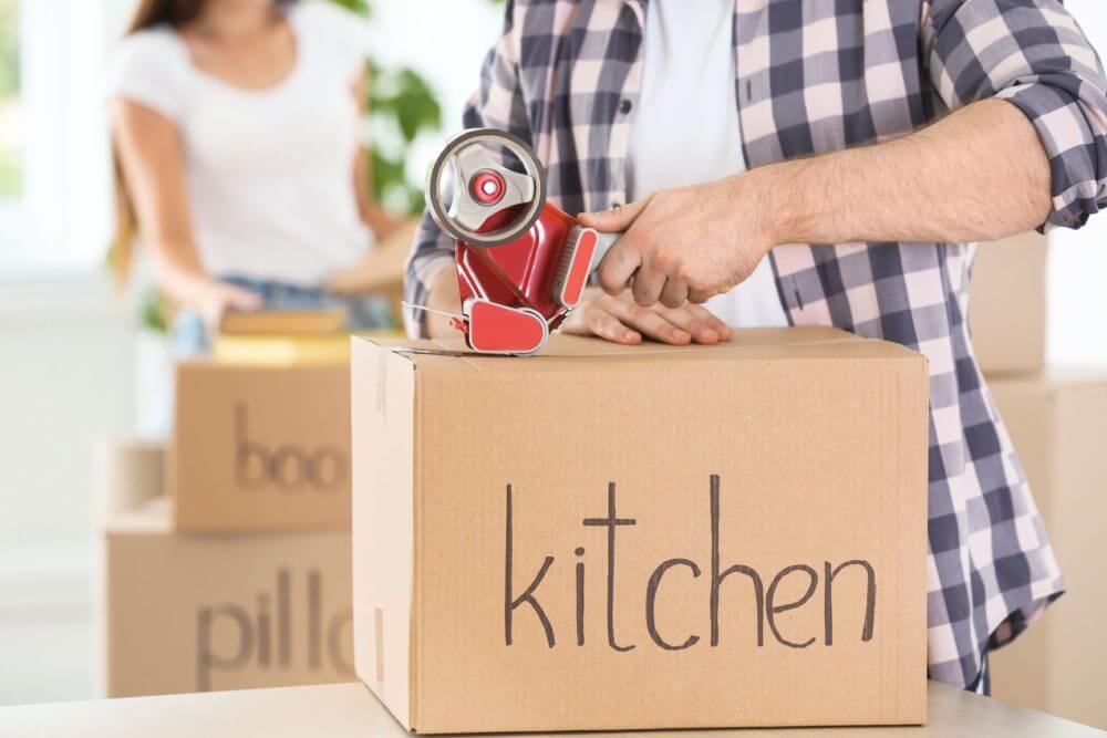 Man taping a box labeled kitchen