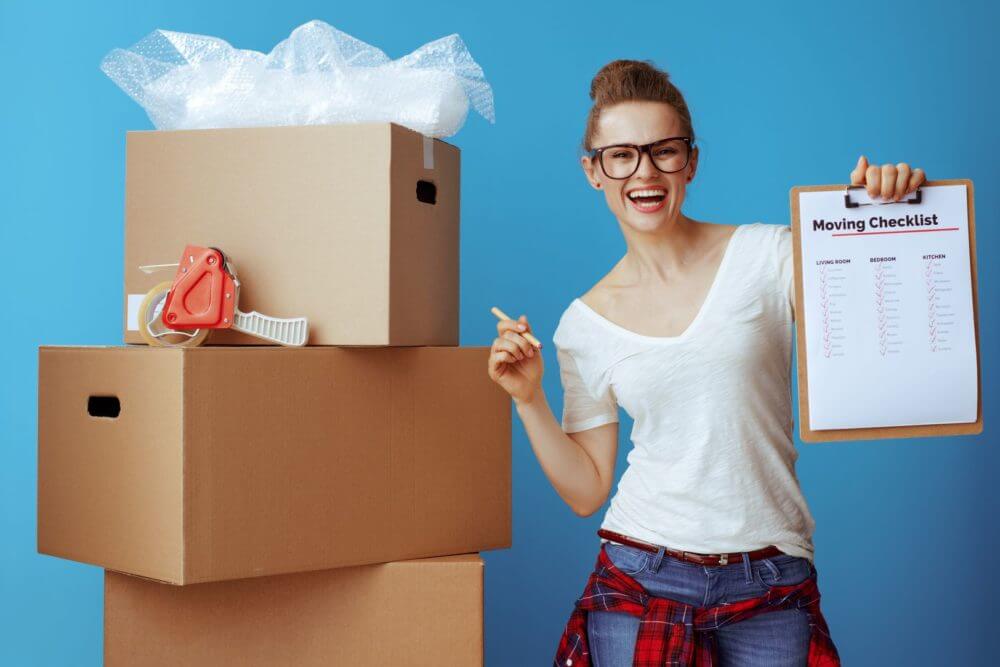 A happy girl standing next to a pile of boxes before long-distance moving company comes