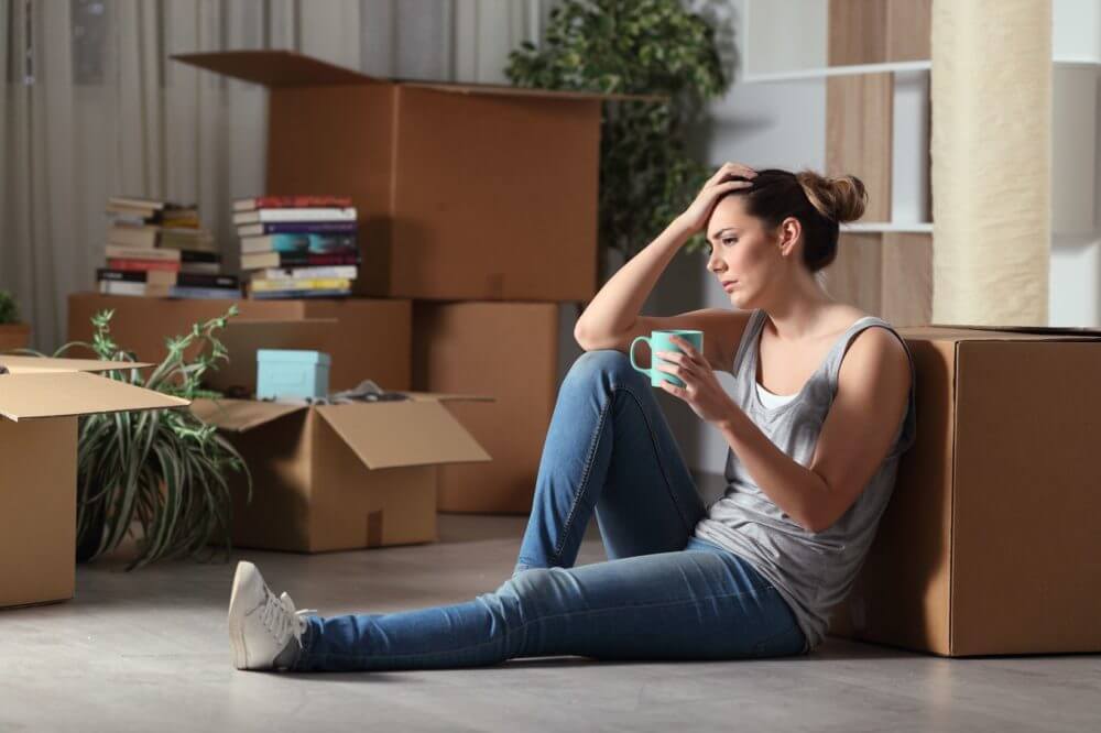 A stressed girl sitting next to a box for long-distance moving