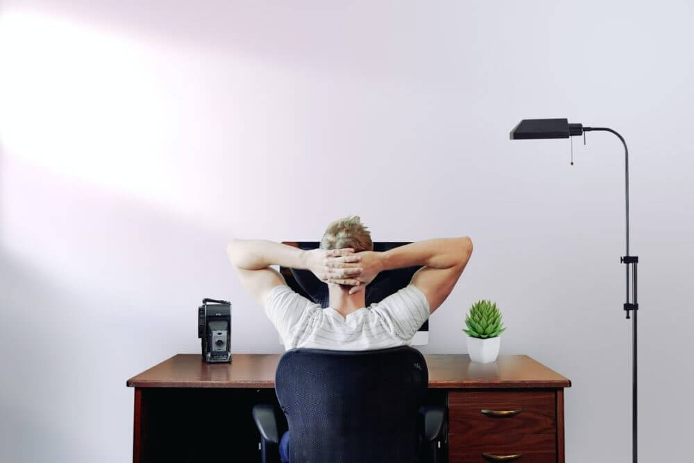 Man with hands behind his head in front of a laptop