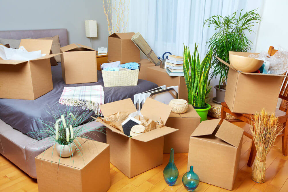 A bunch of nearly packed boxes surrounding a bed in a bedroom