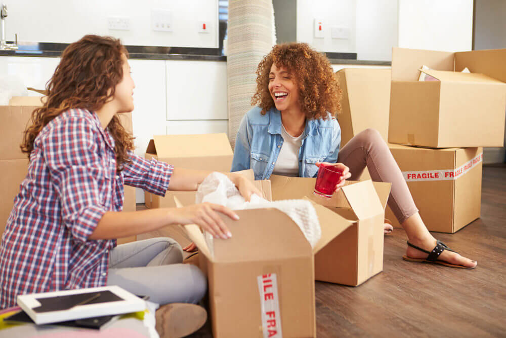 Two women sitting on a floor packing before cross-country moving 