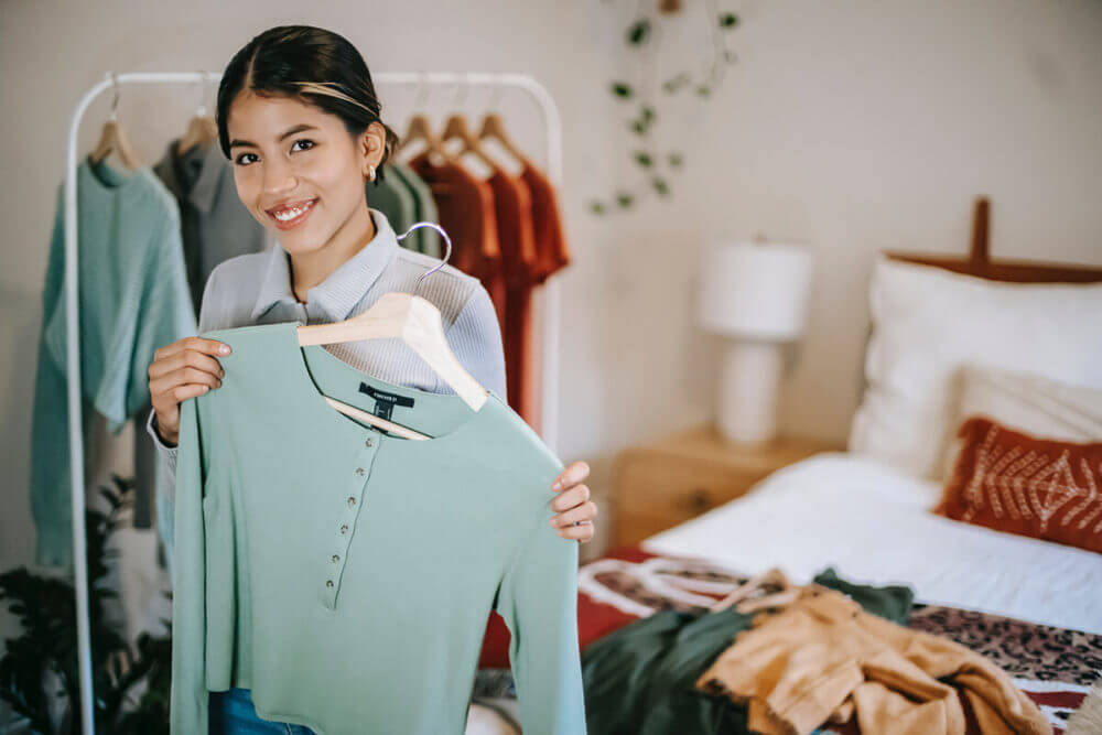 A smiling girl holding a sweater on a hanger