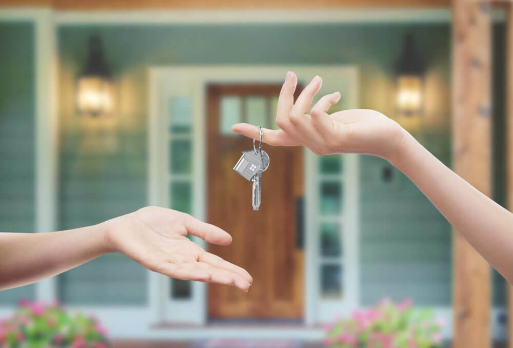 girl is holding the keys in front of the house and handing them over to another resident