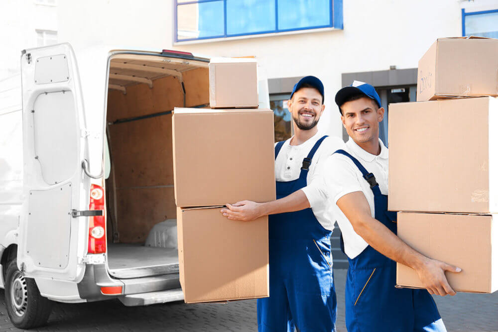 Two cross country movers carrying packages in the living room with a yellow sofa behind them