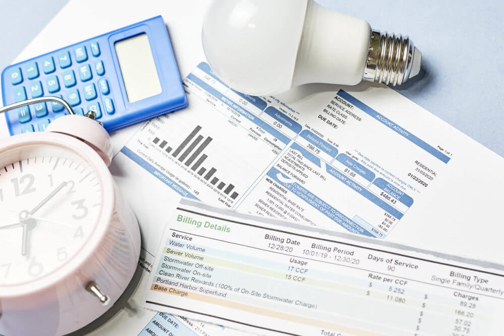 Some bills, a lightbulb, a calculator, and a clock on a desk