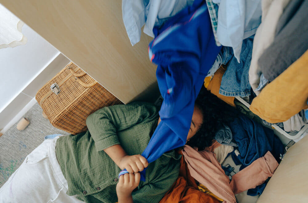 A girl near her close with a pile of clothing over her preparing for long-distance moving