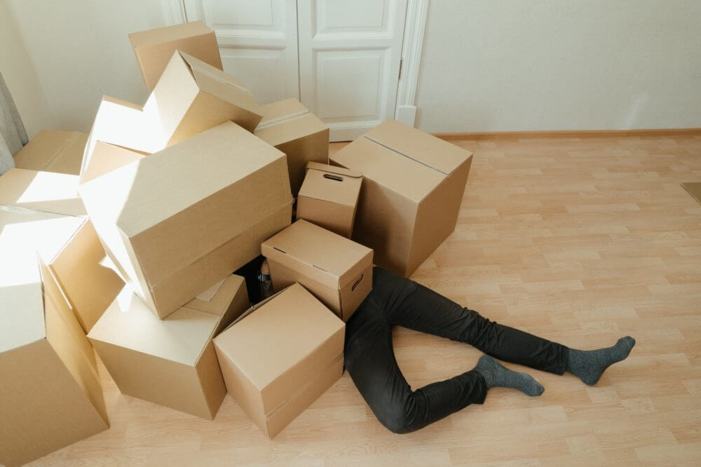 A man stressed about long-distance moving lying under a pile of boxes 