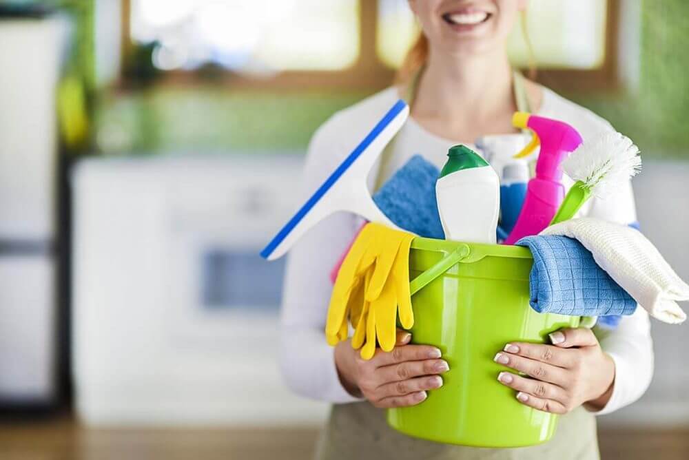 a girl holding a bucket full of cleaning supplies