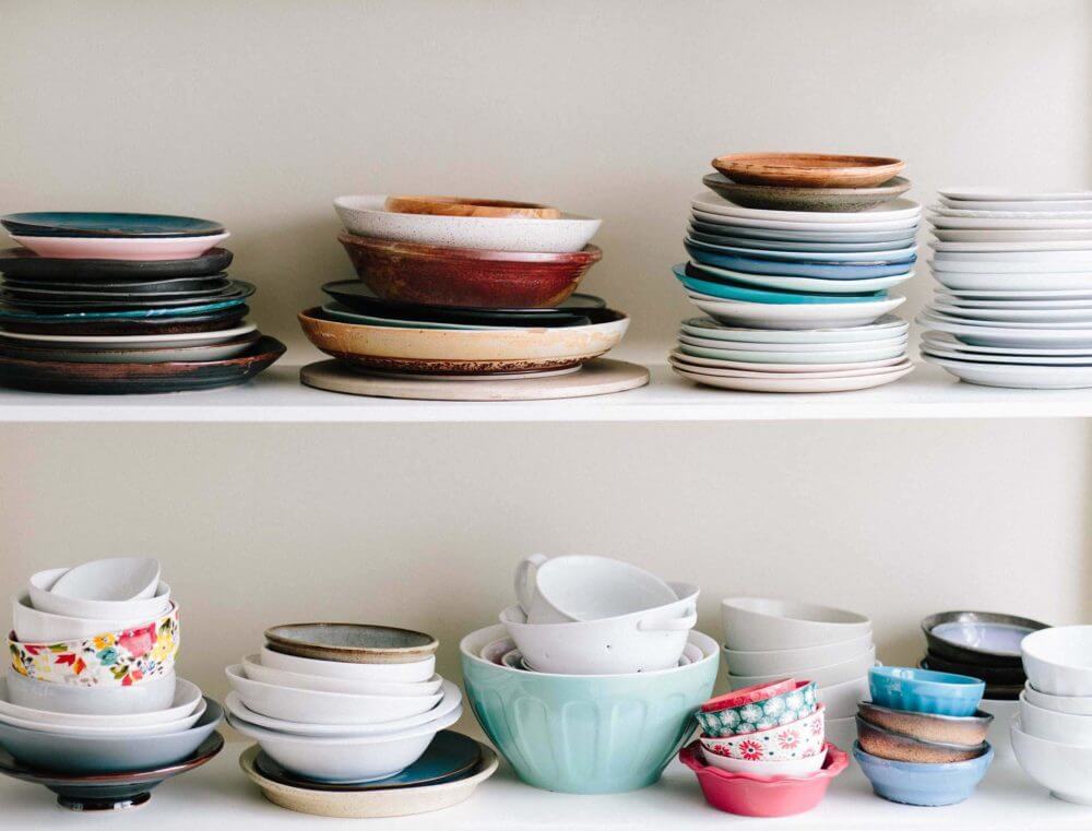 many colorful dishes stacked on two white shelves on top of each other