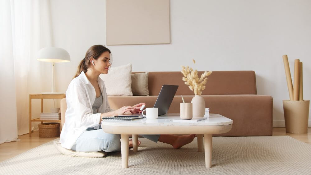 a woman using her laptop and sitting on the floor next to a beige couch