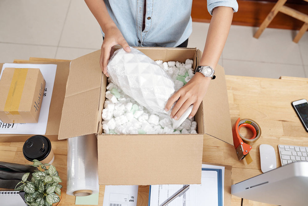 A woman packing a vase in the box full of packing peanuts