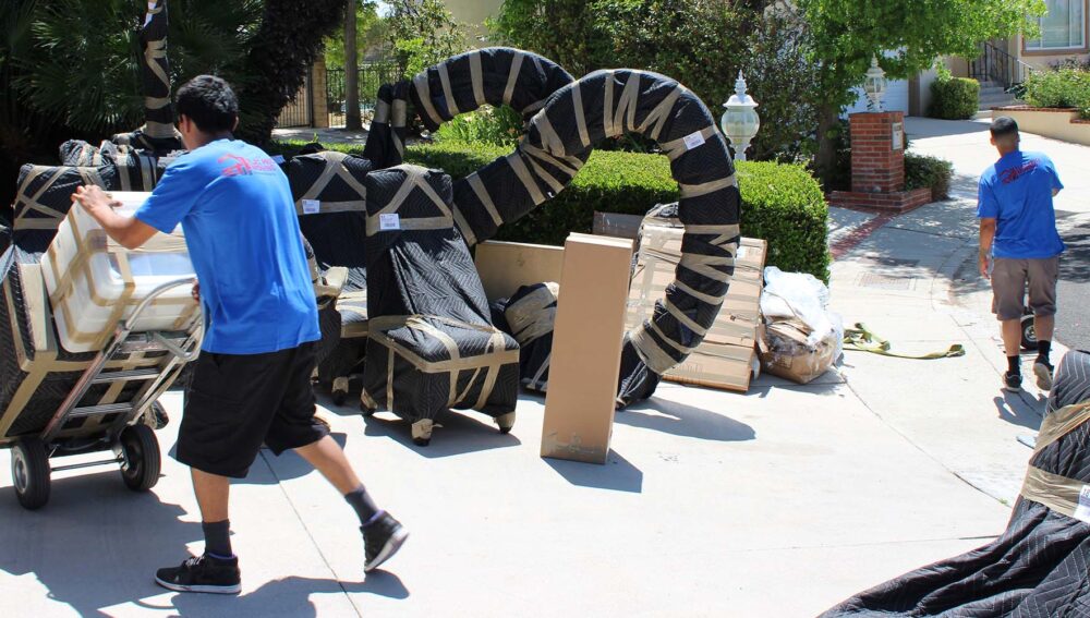 Cross country movers are relocating a couch with a woman sitting on it