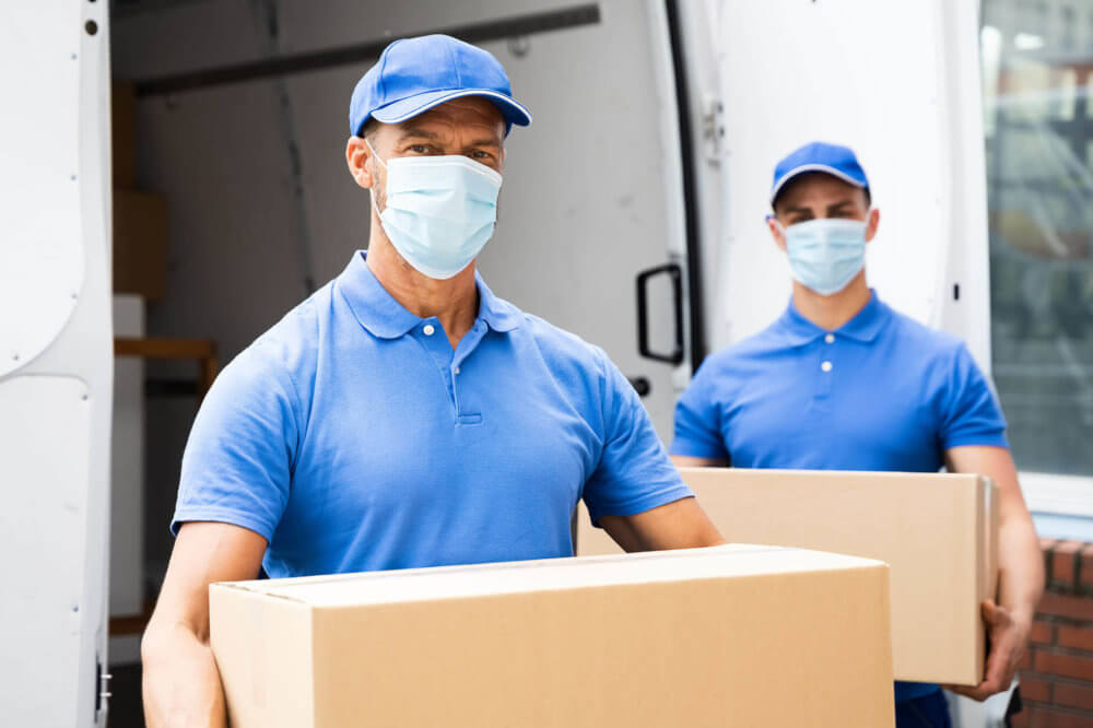 Two cross-country movers holding boxes in front of a van