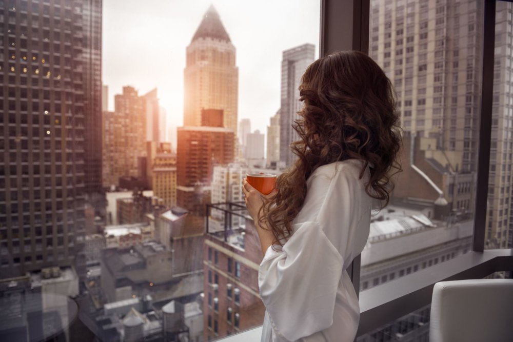 A woman looking out the window and holding a cup of coffee