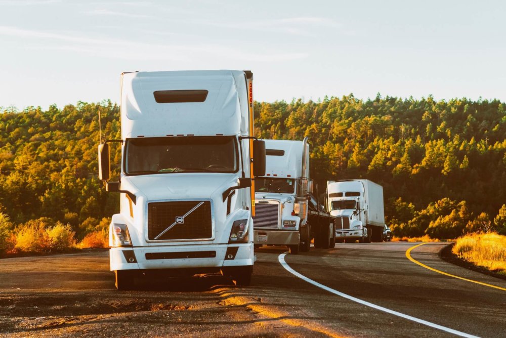 Three white trucks driving on the highway