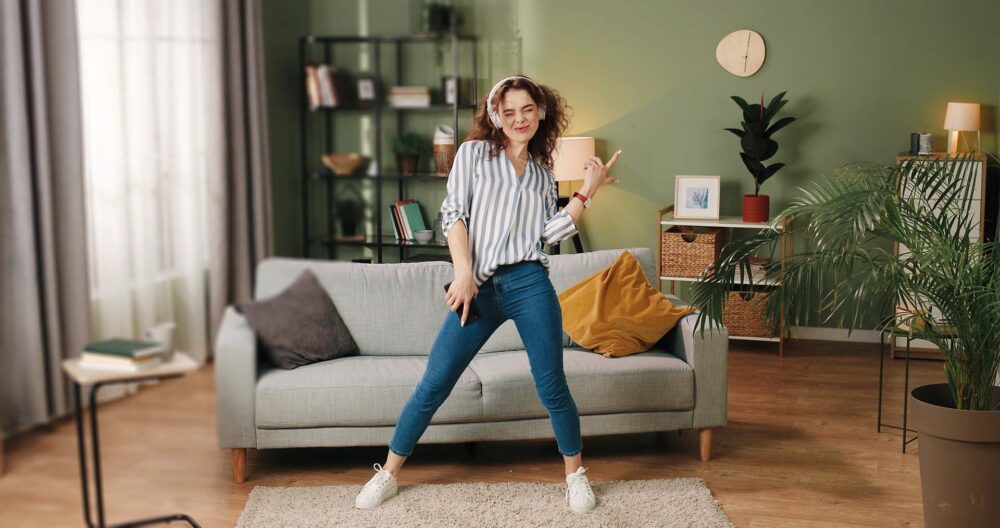 Happy woman with headphones dancing in her living room 