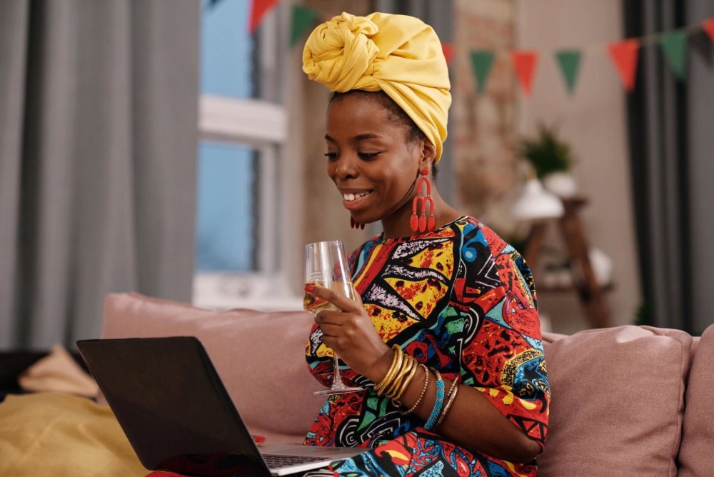 A well-dressed woman smiling at her laptop and holding wine