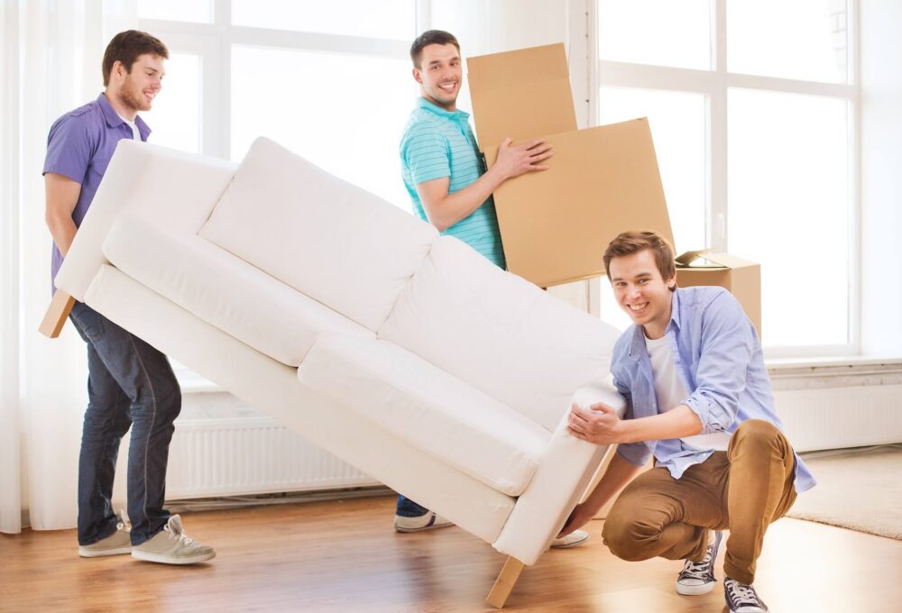 Two guys carrying a sofa, and one guy carrying boxes
