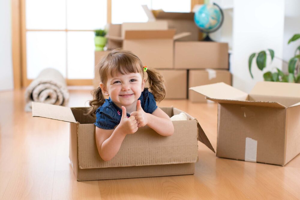 Moving to new apartment. Happy child girl in cardboard box.