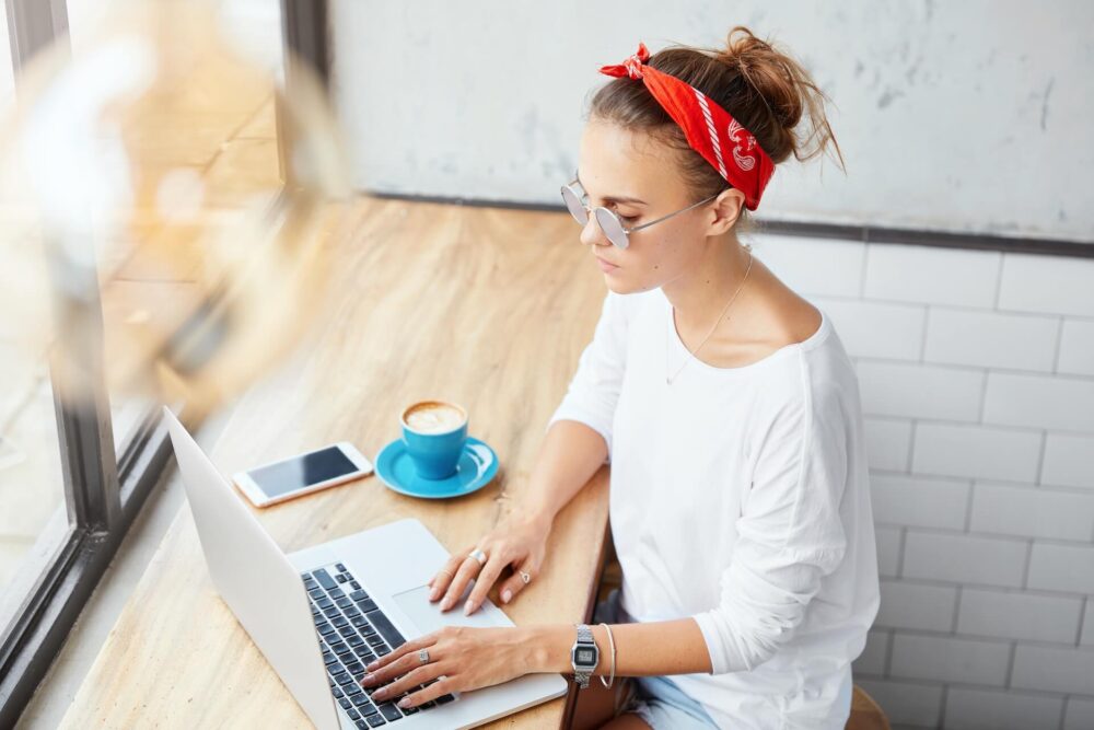 Woman in a cafe, typing on the laptop, coffee, and phone next to her