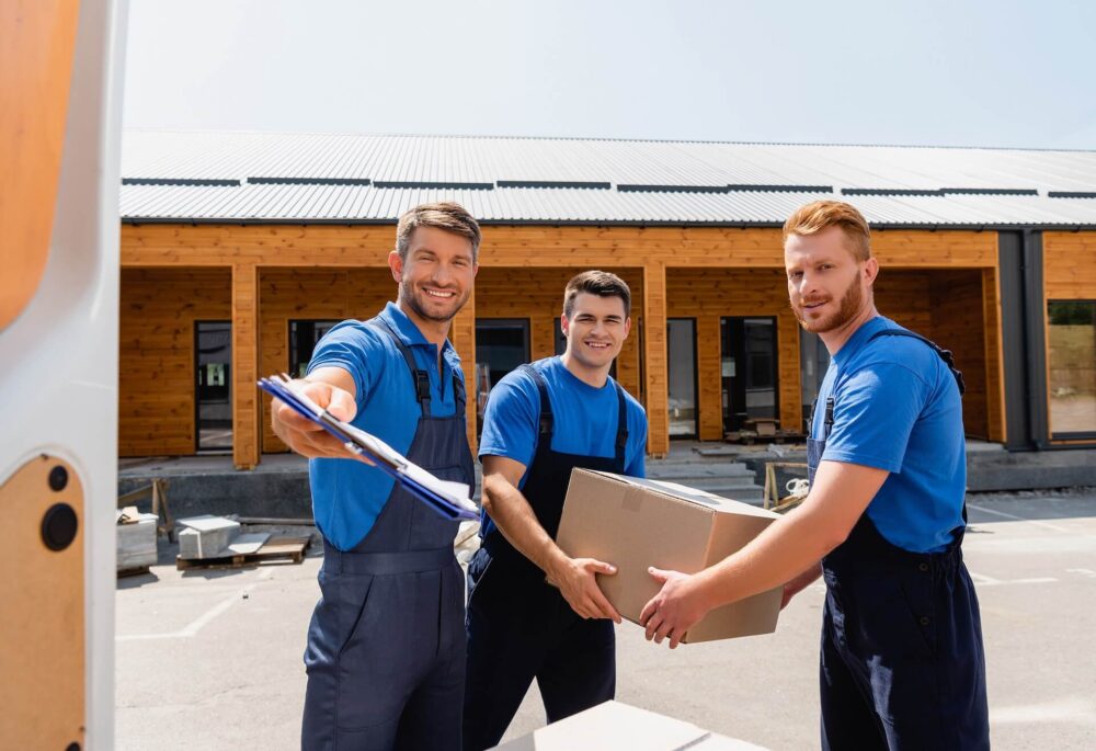 Three cross-country movers smiling while loading a van