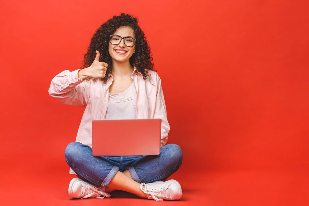 Happy young curly beautiful woman sitting on the floor with a laptop