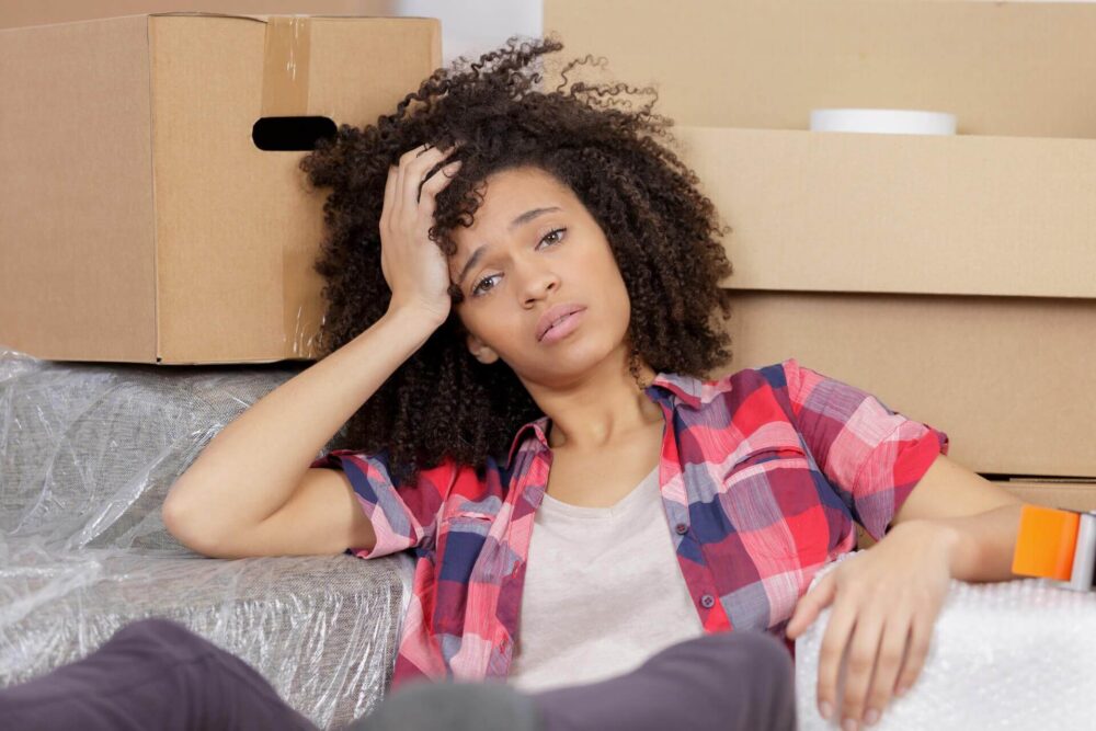 A stressed woman sitting next to the boxes for cross-country moving 