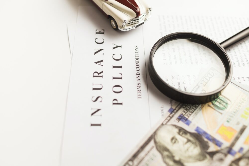 Insurance policy, dollar bill, magnifier, and a small car