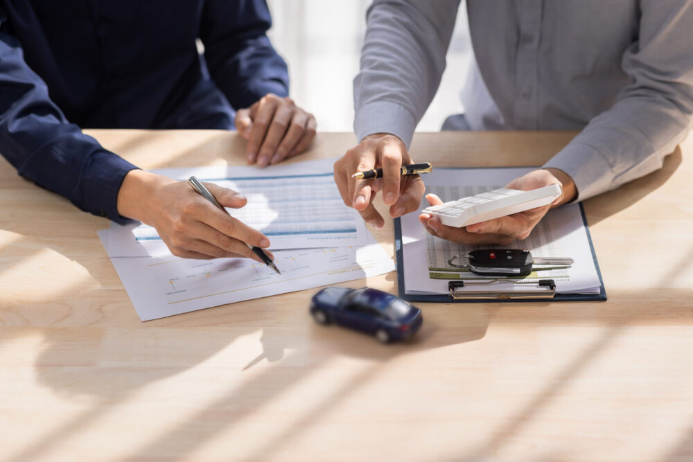 Two people looking at car papers, a small car, and car keys 