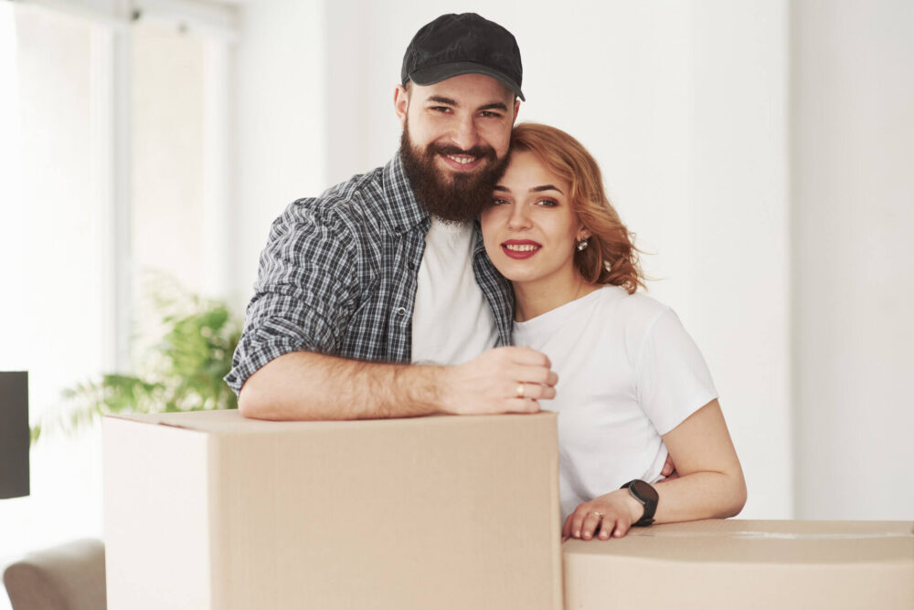 A smiling couple standing in front of the boxes for long-distance moving 