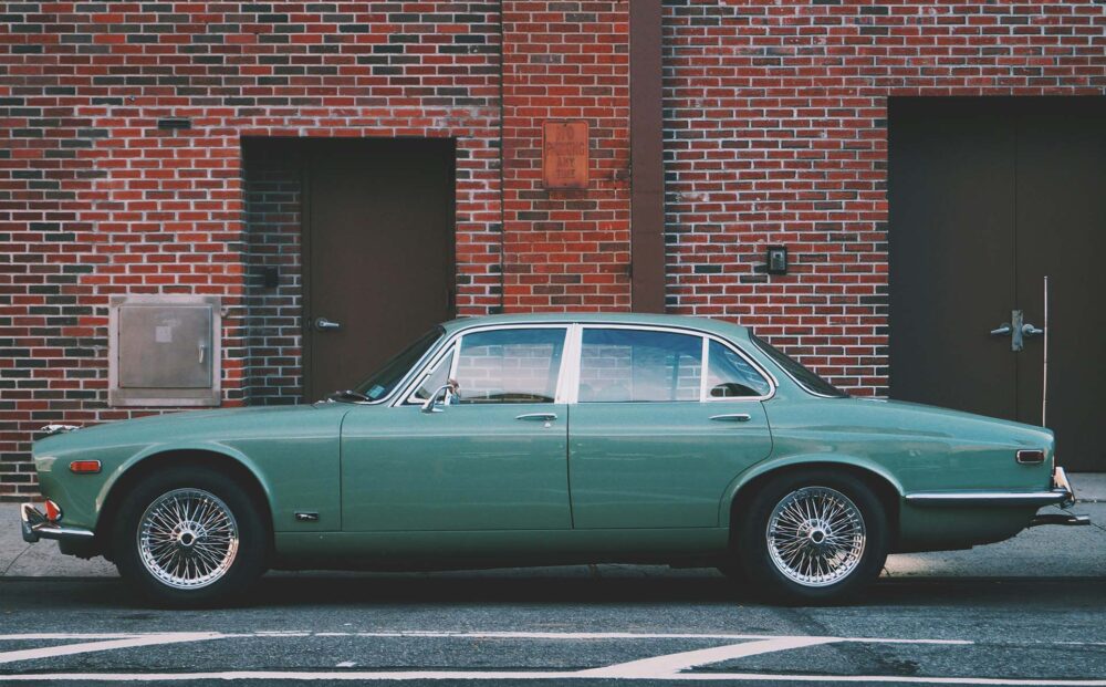 A teal vintage car parked in front of a brick building