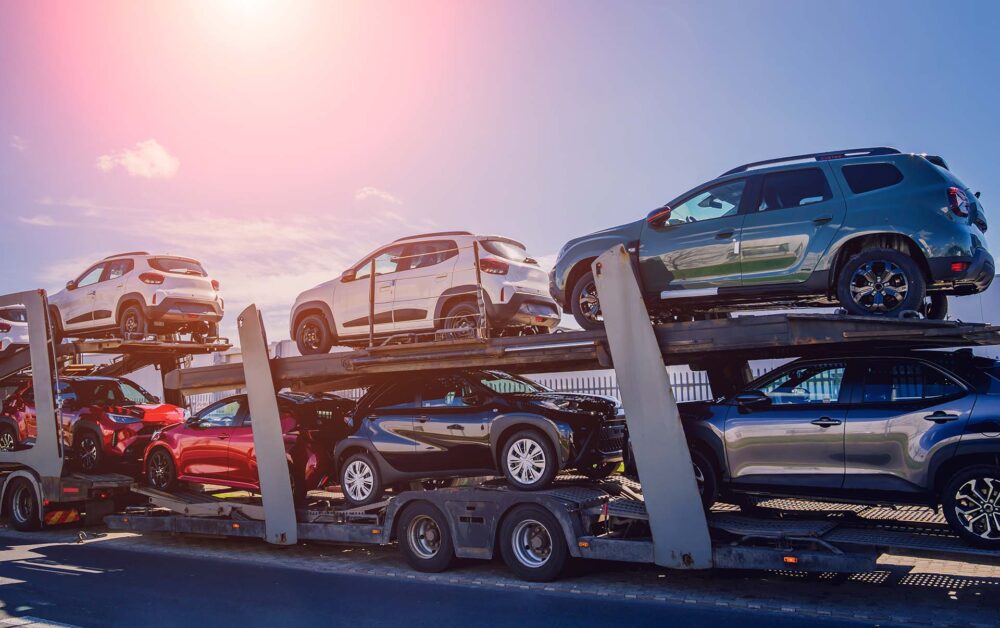 Car carrier trailer transports cars on highway at blue sky background