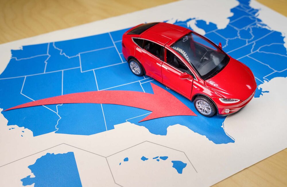 Red Tesla Model X toy car over a USA map and a red arrow from California to Texas