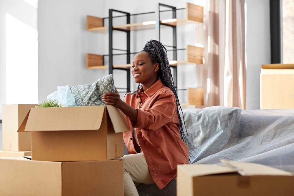 A happy smiling woman unpacking boxes sitting on the sofa at a new home