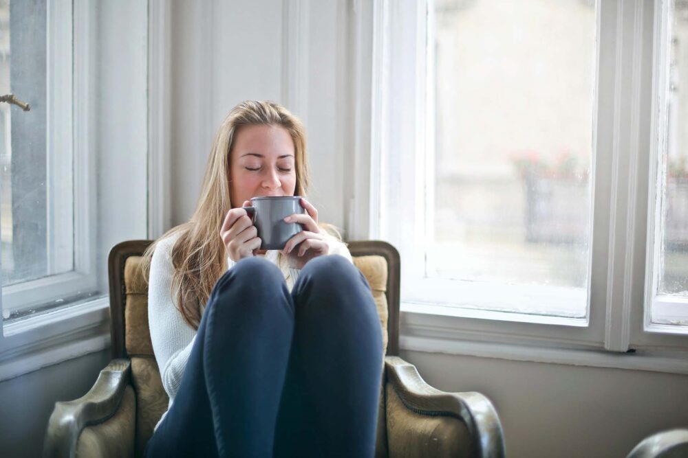 A woman sitting next to a window and drinking coffee