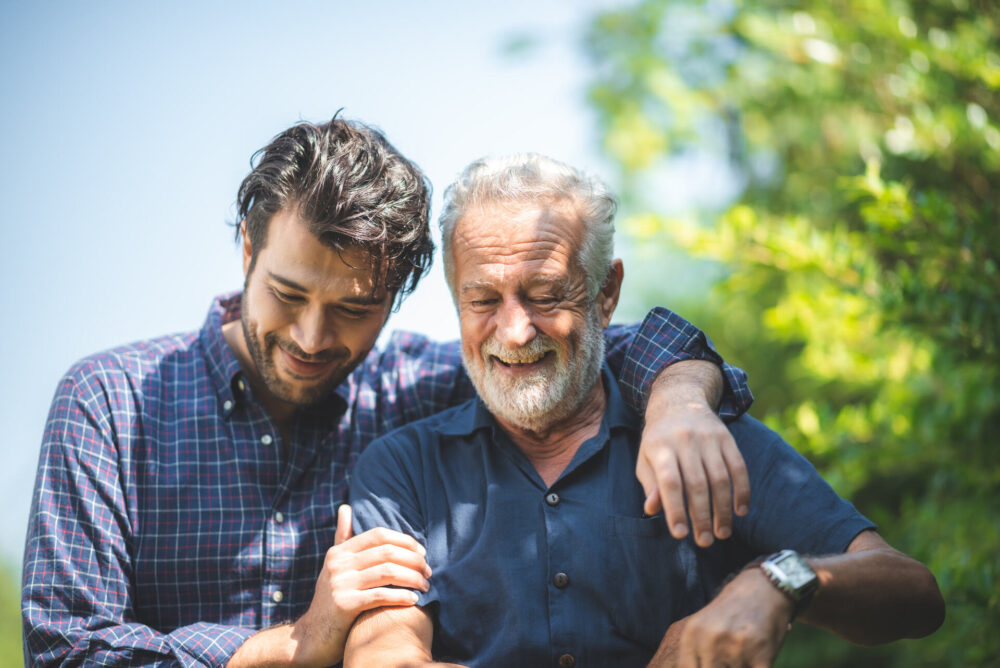 A young man and his father smiling and hugging each other