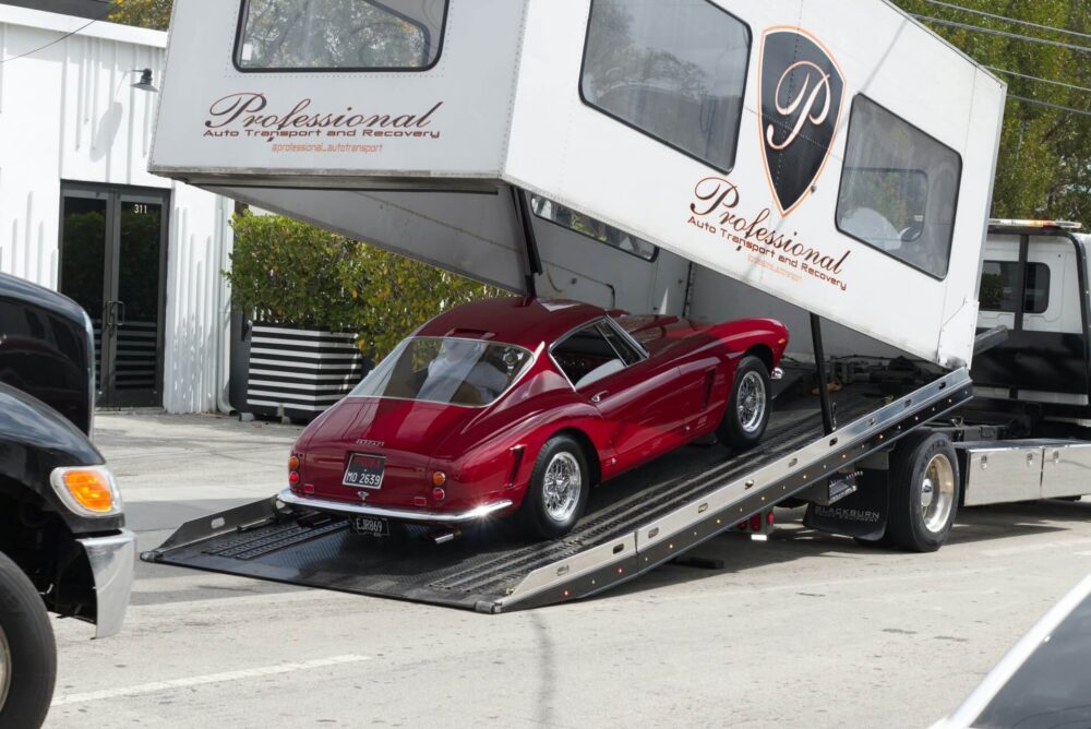 Red vintage car being loaded onto an open car carrier truck for transport.